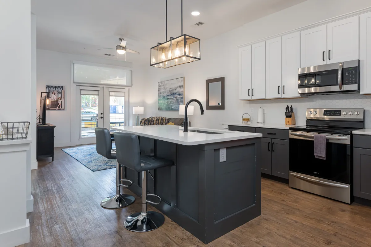 A bright, modern kitchen with a spacious island at its center, gleaming stainless steel appliances, and elegant lighting fixtures overhead. The countertops are uncluttered, inviting both cooking and socializing. The overall feel is warm and welcoming, ideal for both morning coffee routines and evening gatherings.