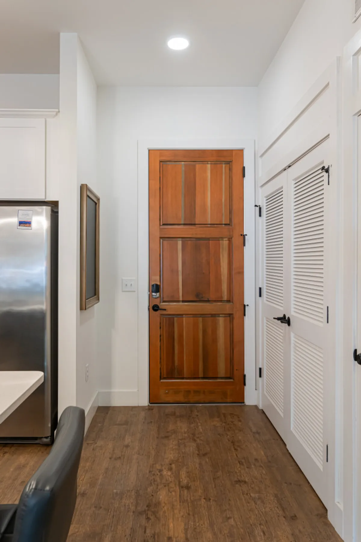 This image features the entryway of the condo, including a sturdy wooden door, a glimpse of the kitchen appliances beyond, and a framed piece of artwork on the wall. The scene gives a subtle preview of the home’s welcoming character and signals a secure, private entrance for arrivals.