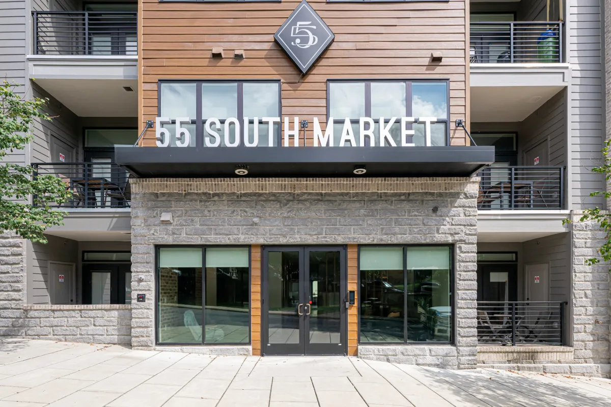 A contemporary building entrance with clear signage and detailed architectural elements, inviting visitors and residents alike. The scene hints at nearby shops, restaurants, and the vibrant community life awaiting just steps outside.