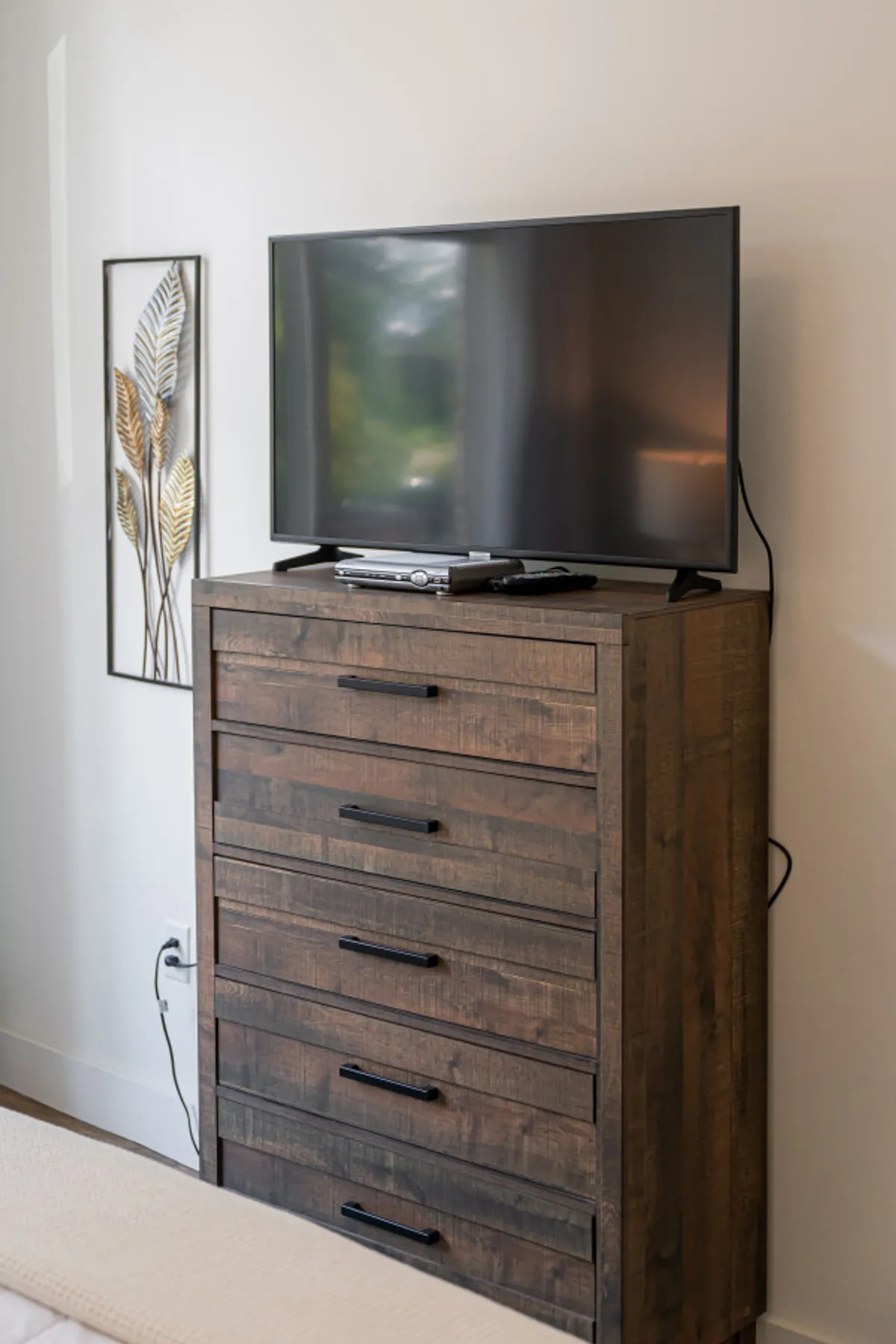 A cozy corner of the bedroom with a wooden dresser, flat-screen TV, and tasteful wall art, offering both storage and a spot to unwind. The setup is both functional and inviting, enhancing the private and comfortable feel of the suite.
