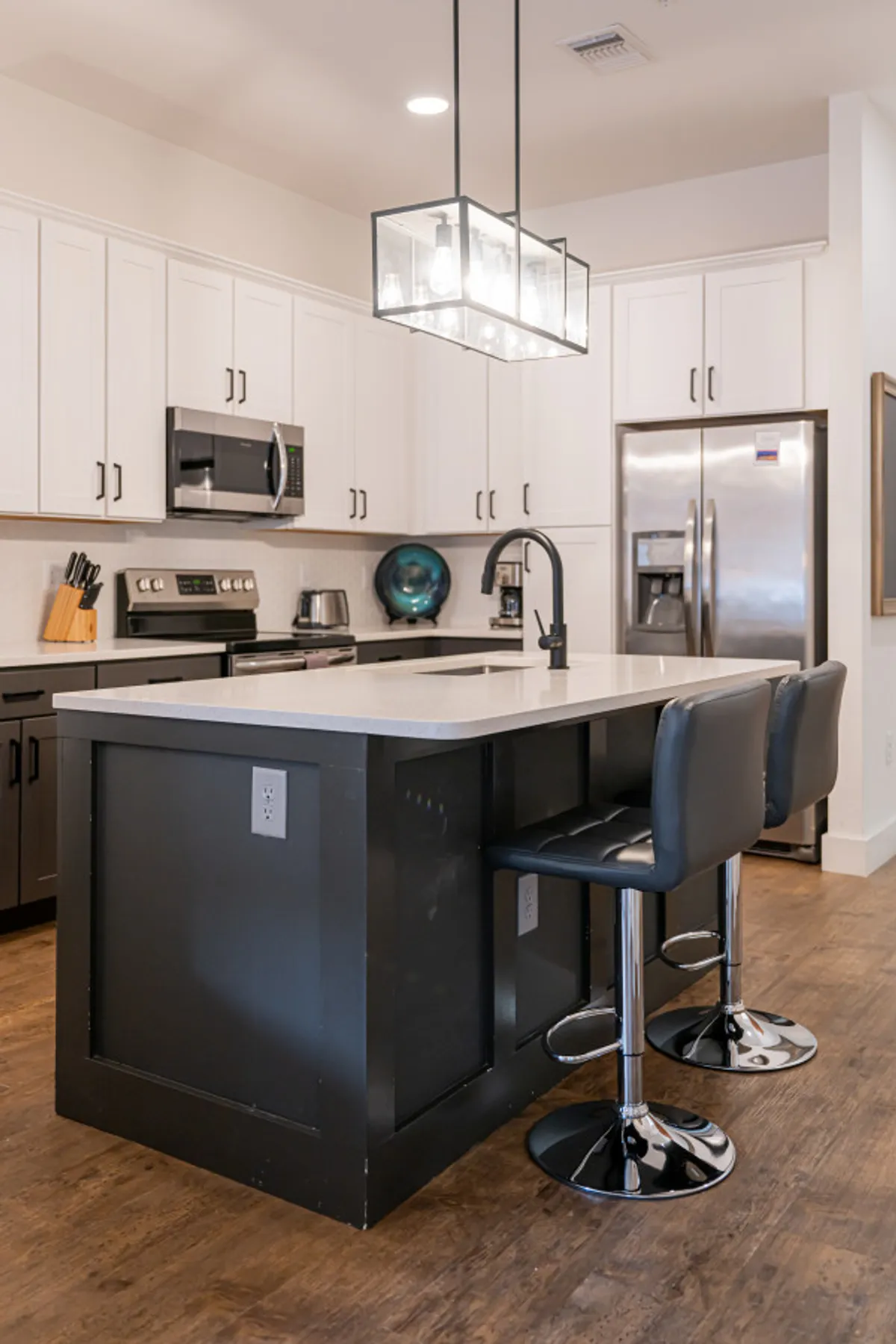 A chic kitchen scene featuring a sleek island with black and silver bar stools, pendant lights, and a contemporary layout. The space encourages casual dining and social connection, with a layout that makes entertaining easy and enjoyable.