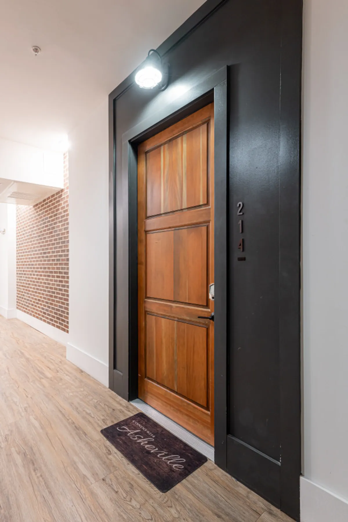 A warm, up-close interior view of an apartment entry door with a visible unit number and welcome mat, hinting at personalized, controlled access to each residence.