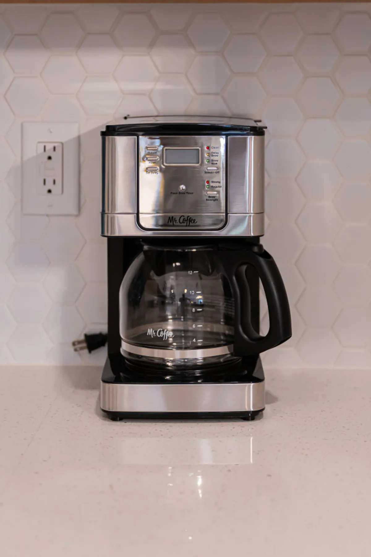 A cozy kitchen corner featuring a coffee maker on a white countertop, set against a stylish hexagonal backsplash. The scene feels welcoming, suggesting the enjoyment of morning routines or unwinding after an evening out.
