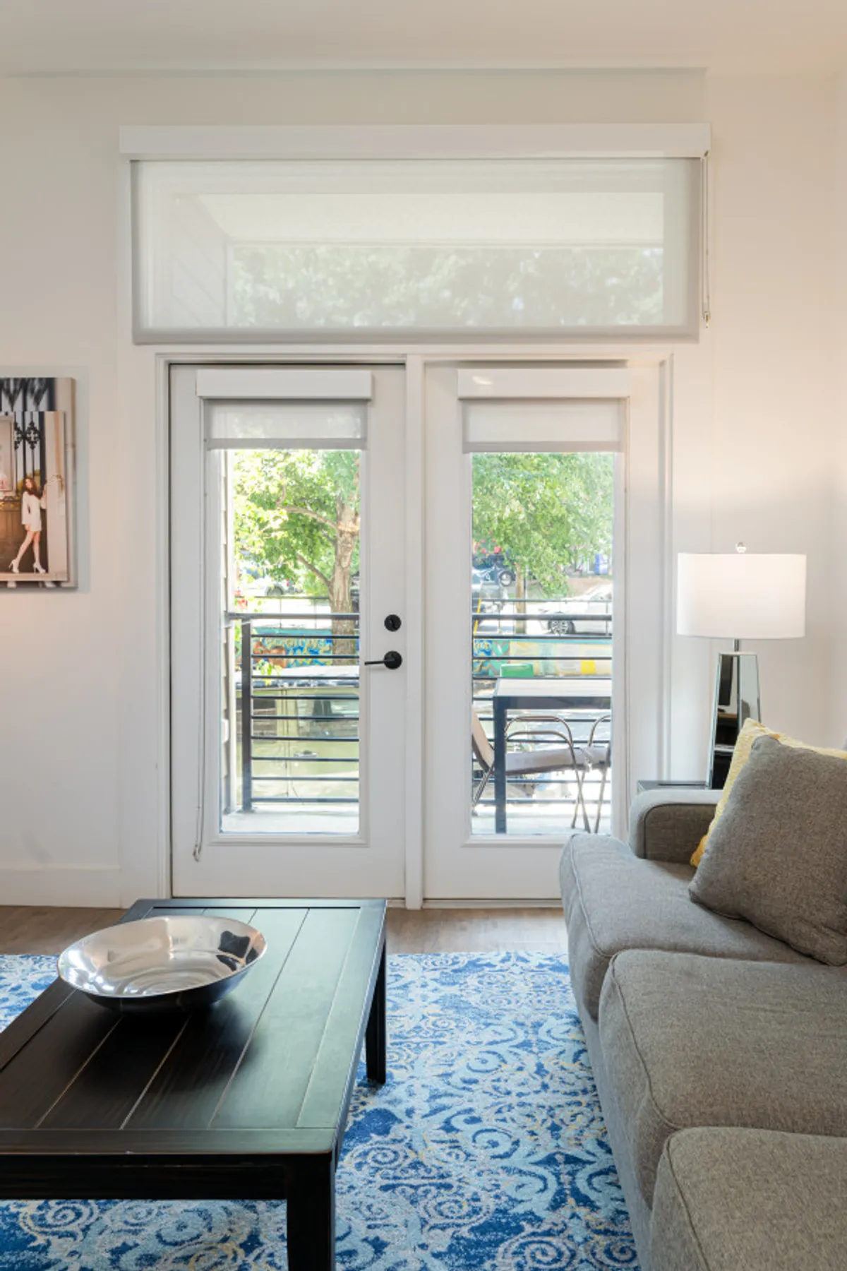 Bright living area with large glass doors opening onto a balcony, a modern sofa, and colorful decor. The indoor-outdoor connection suggests relaxing at home while soaking in the city atmosphere or enjoying urban views from the balcony.