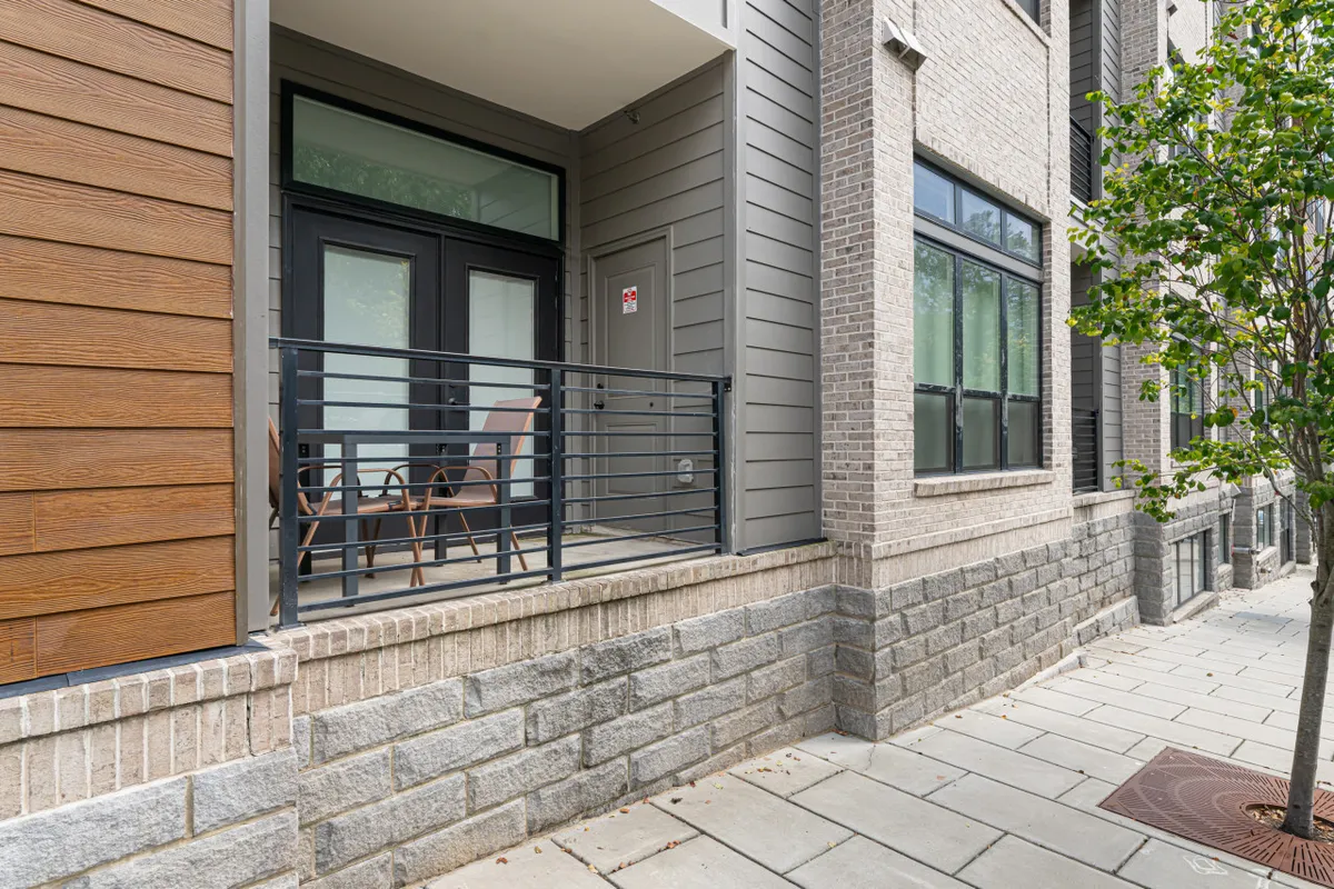A stylish condo porch area with comfortable seating, modern railing details, brick and wood contrasts, and views of landscaped greenery. The setting feels inviting and is ideal for morning coffee or unwinding after a day’s adventures.