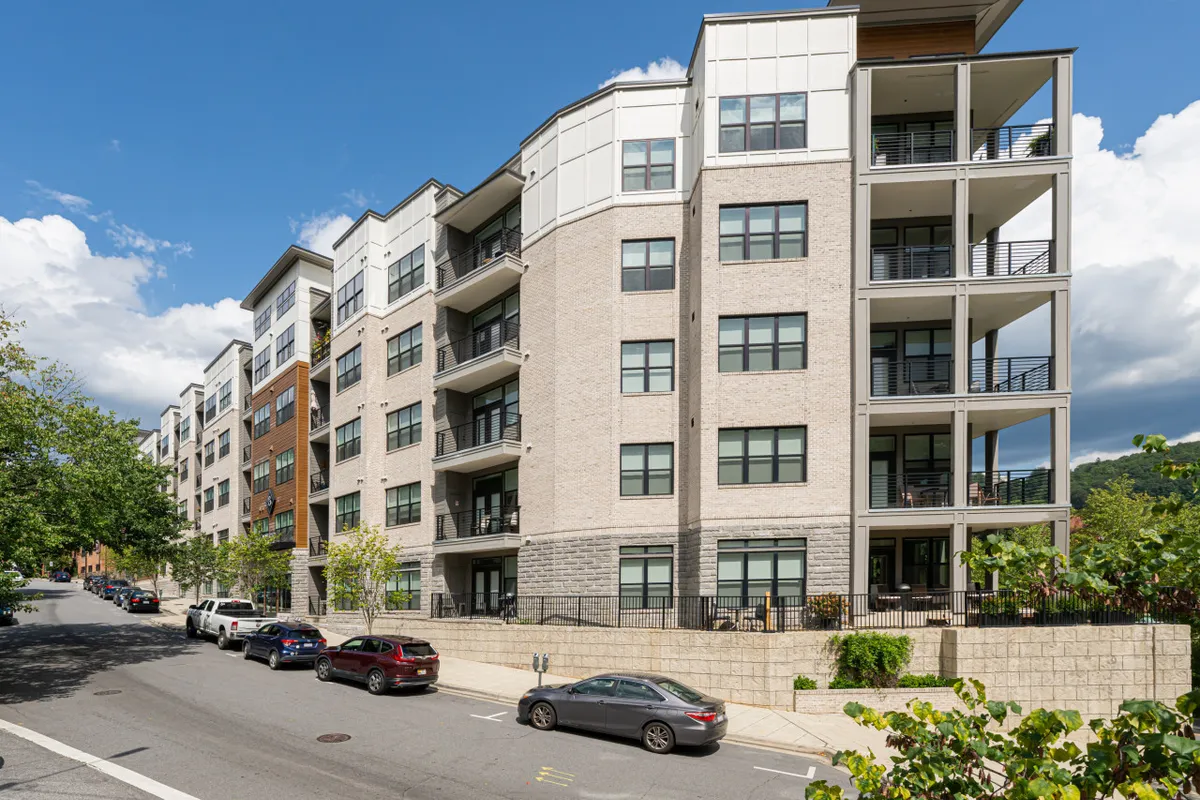 A modern apartment building exterior set in lush green landscaping, featuring balconies with railings. The scene suggests vibrant community living and easy access to leisure time outdoors, embodying the spirit of exploration and neighborhood life.